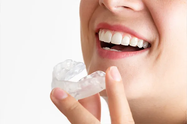 Close-up of a smiling woman holding a clear mouthguard near her teeth, showing how to prevent bruxism. Close-up of a smiling woman holding a clear mouthguard near her teeth, showing how to prevent bruxism.