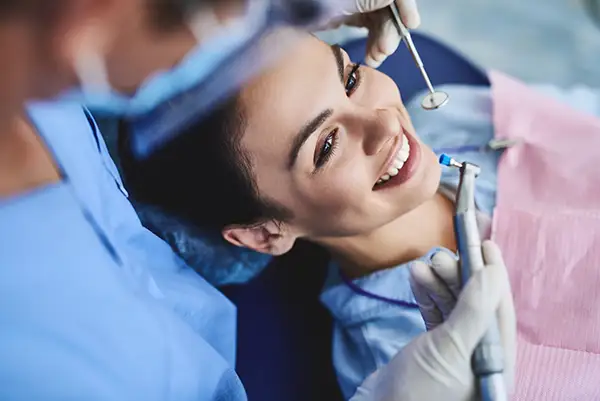 A woman smiling while undergoing a dental cleaning procedure performed by a dentist in a clinic. A woman smiling while undergoing a dental cleaning procedure performed by a dentist in a clinic.