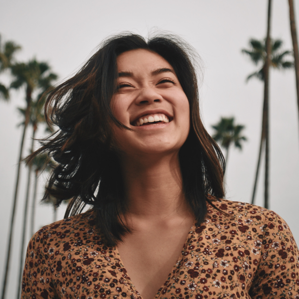 Young woman laughing outdoors with palm trees in the background